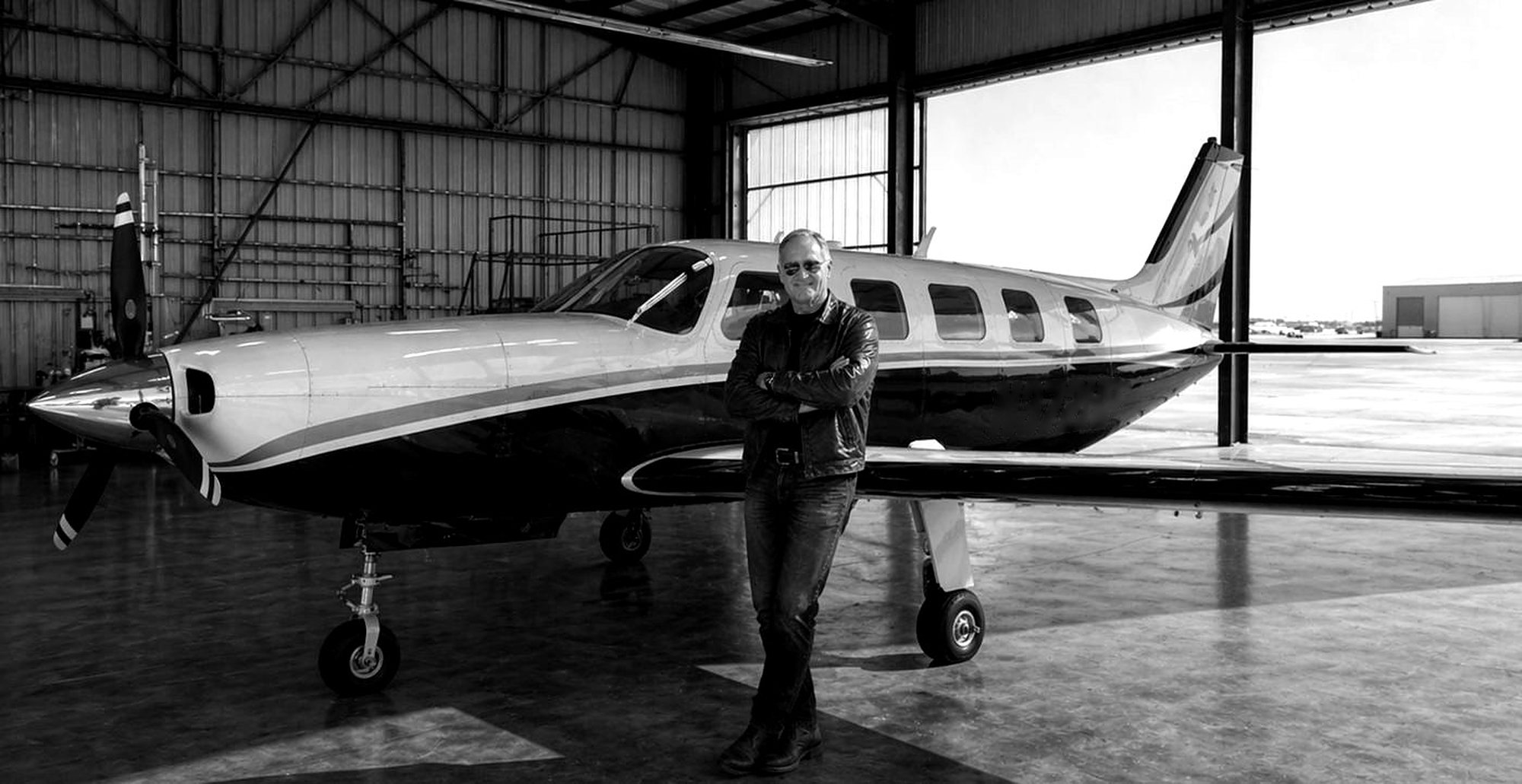 Kevin Seney standing beside his airplane in a hangar, black and white