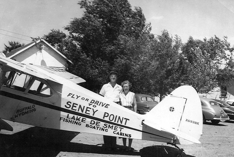 Ruth and Frank Seney standing beside a Piper Cub lettered Seney Point, Lake De Smet